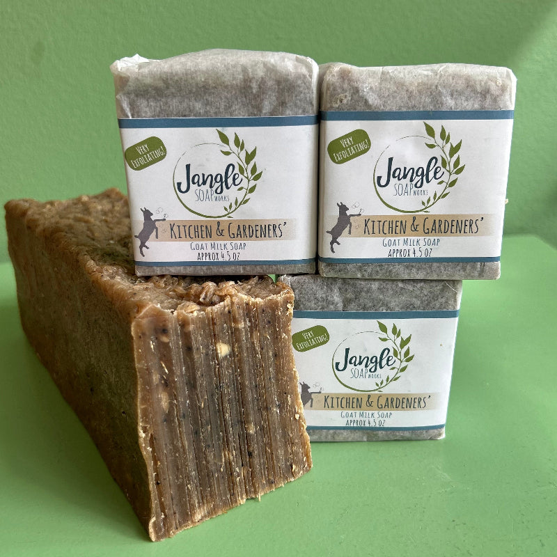 Three wrapped bars of kitchen and gardeners soap by Jangle Soap Works.  The bars are on a green background with a bulk loaf of soap showing the exfoliating details in the soap. 