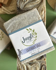 Jangle Soaps Lavender Sage Goat's Milk Soap wrapped in white paper and on top of a bulk loaf of the same soap.