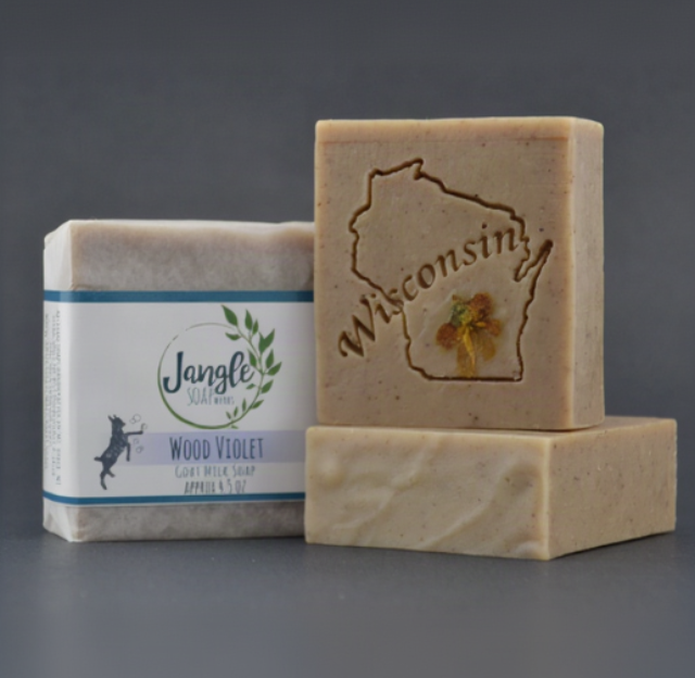 Jangle's Wood Violet Soap. The Tan bar  is stamped with an image of a Wisconsin and a dried wood violet. Two bars are unwrapped and one is upright on top of the other and the third bar is wrapped in paper. 