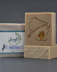 Jangle's Wood Violet Soap. The Tan bar  is stamped with an image of a Wisconsin and a dried wood violet. Two bars are unwrapped and one is upright on top of the other and the third bar is wrapped in paper. 