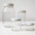 Four empty Container Glass Jars with aluminum caps in different sizes are displayed on a white surface, ideal for storing your DIY creations against a light background.
