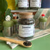 A refillable jar of Jasmine tea. The jar has a cork lid and a bamboo attachable spoon. The spoon is in front of the jar full of jasmine tea. 