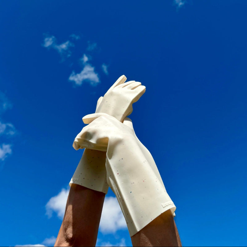 Hands modeling  white silicone kitchen gloves. The sturdy, washable kitchen gloves have grooves on the palm and fingers to make handling wet dishes easy. The hands wearing the gloves are lifted into a blue sky. 