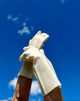 Hands modeling  white silicone kitchen gloves. The sturdy, washable kitchen gloves have grooves on the palm and fingers to make handling wet dishes easy. The hands wearing the gloves are lifted into a blue sky. 