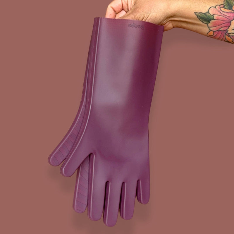 A tattooed hand holds Fig  premium silicone dishwashing gloves on a brown background. 