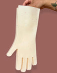 A tattooed hand holds oat speckled sturdy silicone kitchen gloves on a brown background. 