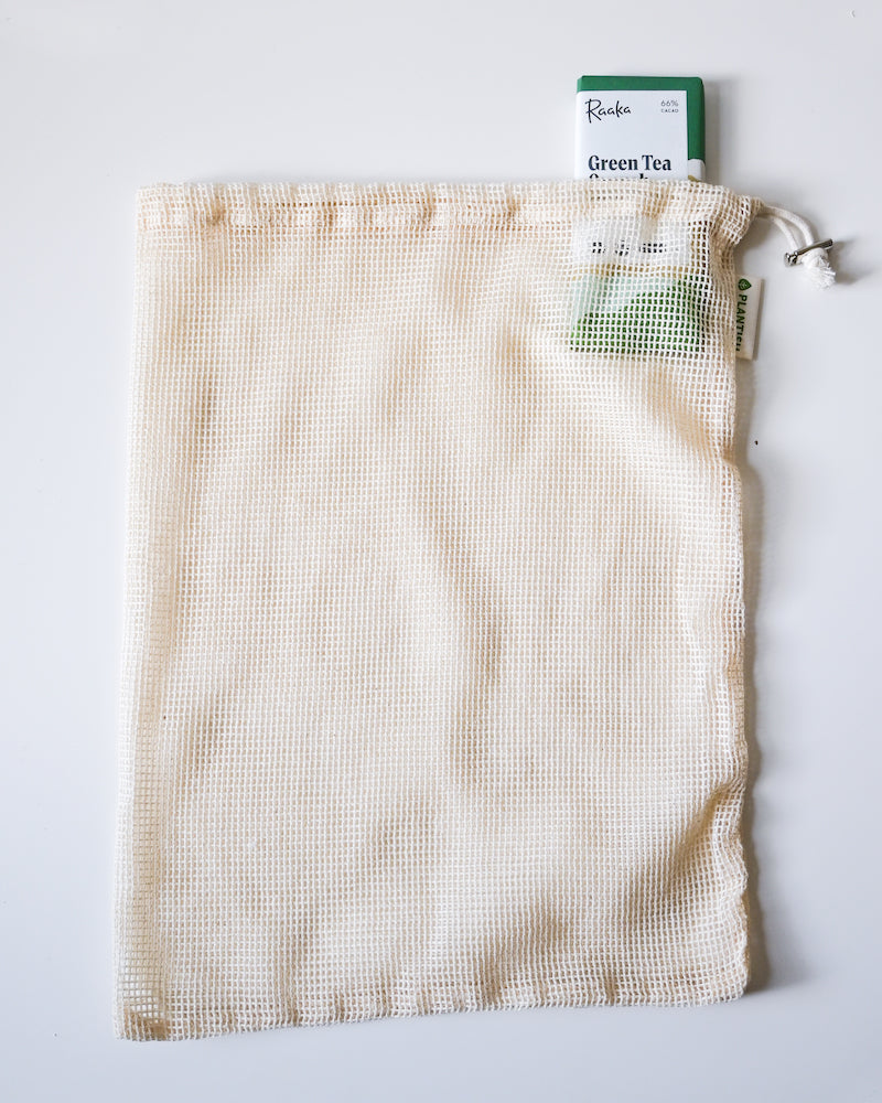 Mesh tea bag with a green tea package on a light gray background