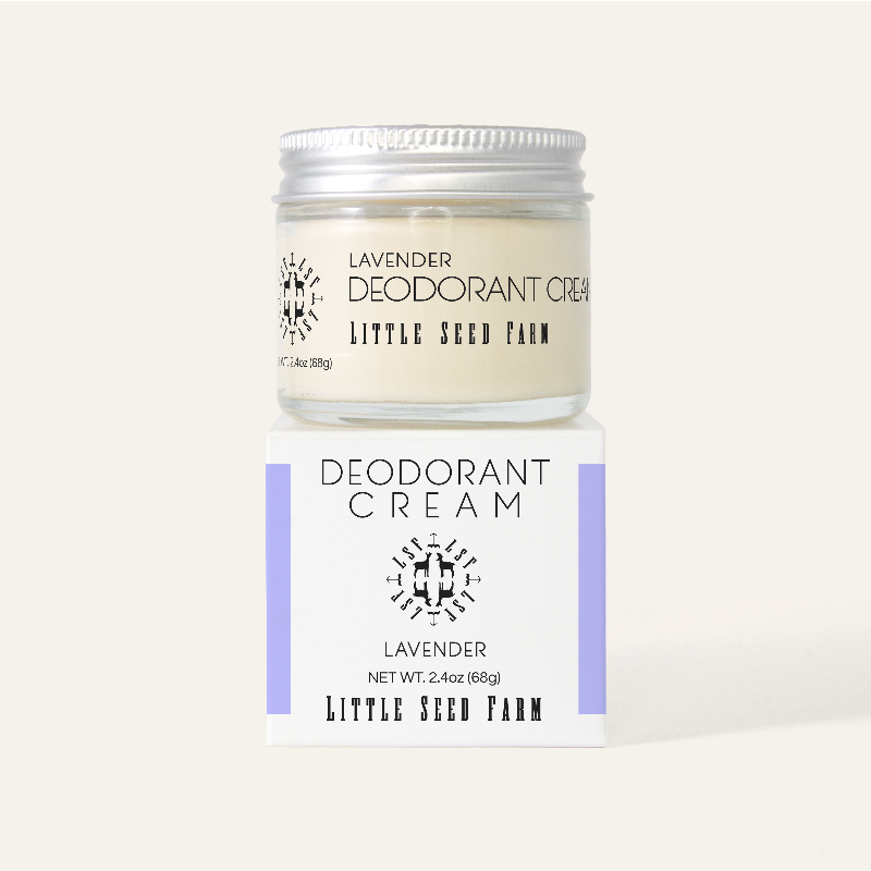 A refillable jar of little seed farm deodorant on top of its white and purple box.