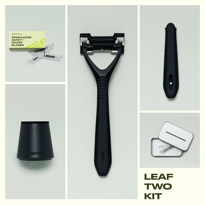 A flat lay of the leaf two razor kit in the color black.  The image shows the contents of the Leaf two razor kit next to the razor is a 50 count refill pack, a matching black stand, a silicone handle sleeve, and a recycling tin.