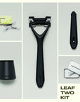 A flat lay of the leaf two razor kit in the color black.  The image shows the contents of the Leaf two razor kit next to the razor is a 50 count refill pack, a matching black stand, a silicone handle sleeve, and a recycling tin.