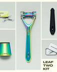 A flat lay of the leaf two razor kit in the color prism.  The image shows the contents of the Leaf two razor kit next to the razor is a 50 count refill pack, a matching prism stand, a silicone handle sleeve, and a recycling tin.