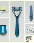 A flat lay of the leaf two razor kit in the color glacier.  The image shows the contents of the Leaf two razor kit next to the razor is a 50 count refill pack, a matching glacier stand, a silicone handle sleeve, and a recycling tin.