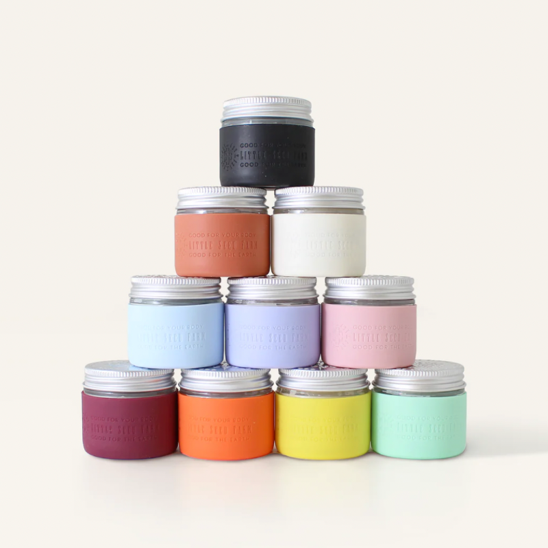 A pyramid of ten pastel or muted Deodorant Cream jars with silver lids by Little Seed Farm, handmade in Tennessee, is arranged on a plain light background.