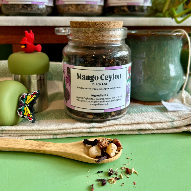 A refillable jar full of Mango Ceylon tea. The jar has a cork lid and an attachable spoon. 