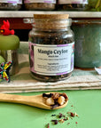 A refillable jar full of Mango Ceylon tea. The jar has a cork lid and an attachable spoon. 
