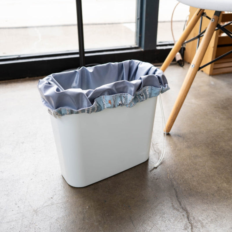 A small trash bin with a grey drawstring reusable pail liner in it. 