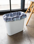 A small trash bin with a grey drawstring reusable pail liner in it. 