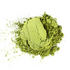 A mound of Mountain Rose Herbs Matcha Powder sits on a white surface, with fine green powder dusted around the main pile.