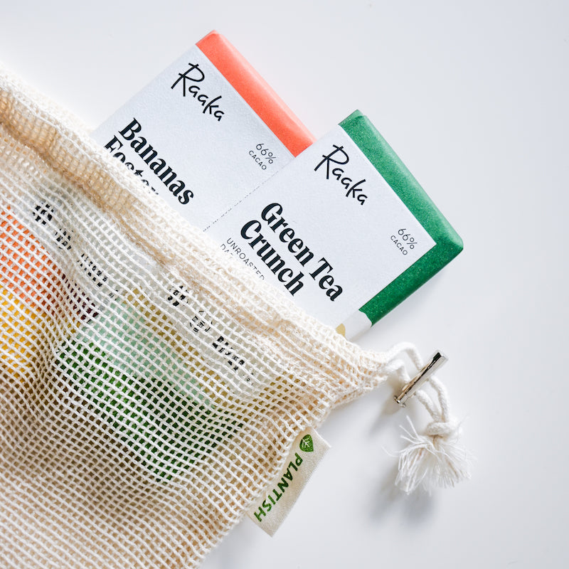 Three bars of soap labeled 'Raaka' with a mesh bag on a white background