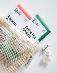 Three bars of soap labeled 'Raaka' with a mesh bag on a white background