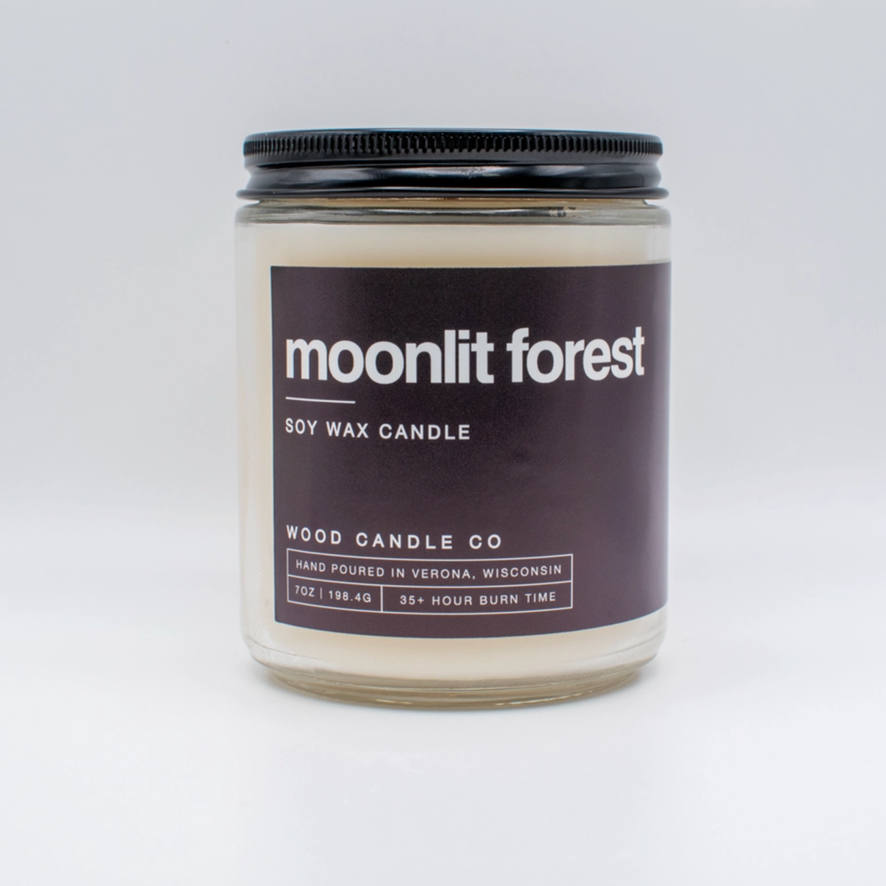 glass candle jar with black label "moonlit forest" on white backdrop