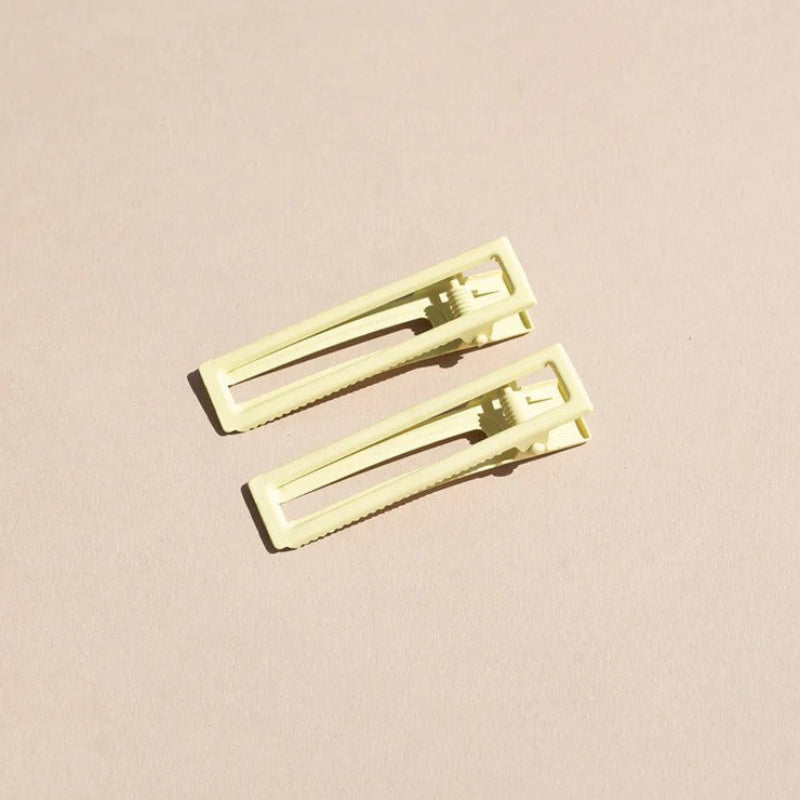 Two wide metal hair clips in light yellow. The clips are sitting on a beige background. 