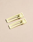 Two wide metal hair clips in light yellow. The clips are sitting on a beige background. 