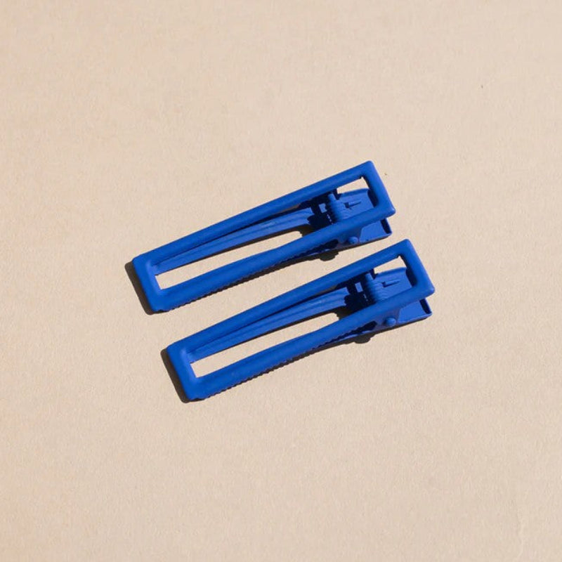Two wide metal hair clips in bright blue. The clips are sitting on a beige background. 