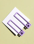 Two wide metal hair clips in a light purple color. The clips are attached to a white card and are sitting on a beige background. 