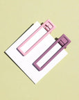 Two wide metal hair clips one is light pink and the other is mauve. The clips are attached to a white card and are sitting on a beige background. 