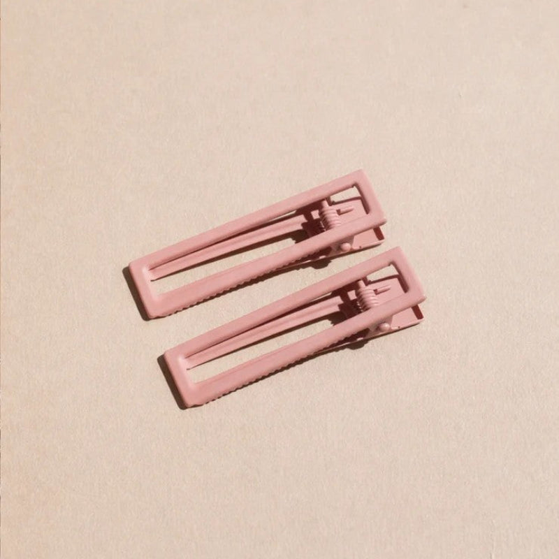 Two wide metal hair clips in light pink. The clips are sitting on a beige background. 