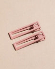 Two wide metal hair clips in light pink. The clips are sitting on a beige background. 
