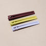 Three metal hair clips in brown, green, and purple on a beige background. 