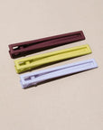 Three metal hair clips in brown, green, and purple on a beige background. 