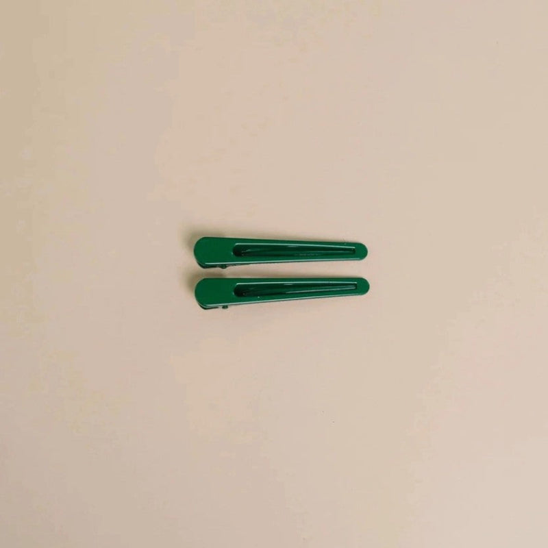 Two Green glossy metal hair clips on a beige background. 