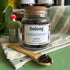 A refillable jar of Oolong tea. The jar has a cork lid and an attachable bamboo spoon. The spoon is in front of the jar full of tea. 