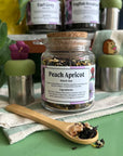 Jar of Peach Apricot black tea with a wooden spoon on a green surface