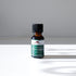 A small brown glass bottle labeled Mountain Rose Herbs Peppermint Essential Oil, 1/2 fl. oz. (15 mL), sits on a white surface with sunlight casting a shadow behind it. This oil is steam distilled for purity and freshness.