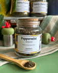 A refillable Jar of peppermint tea. The jar has a cork lid and an attachable bamboo spoon. 