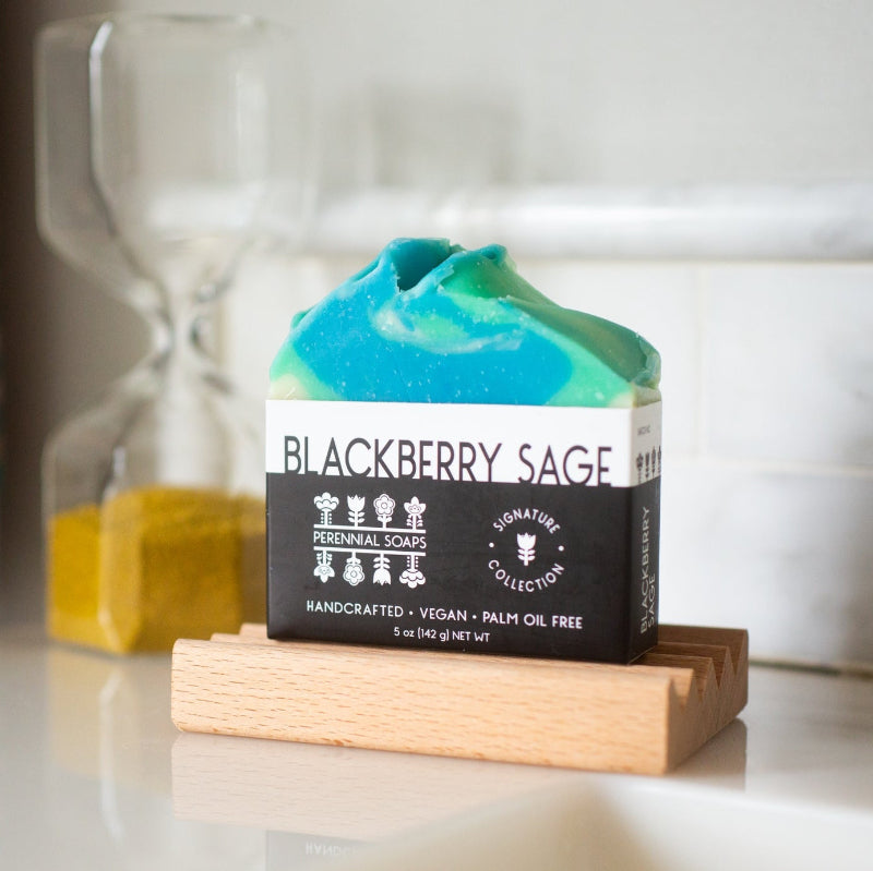 Bar of soap with a label reading 'Blackberry Sage' on a wooden stand.