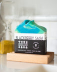 Bar of soap with a label reading 'Blackberry Sage' on a wooden stand.