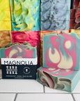 Magnolia Soap bars with a stack of various soap bars behind it. 