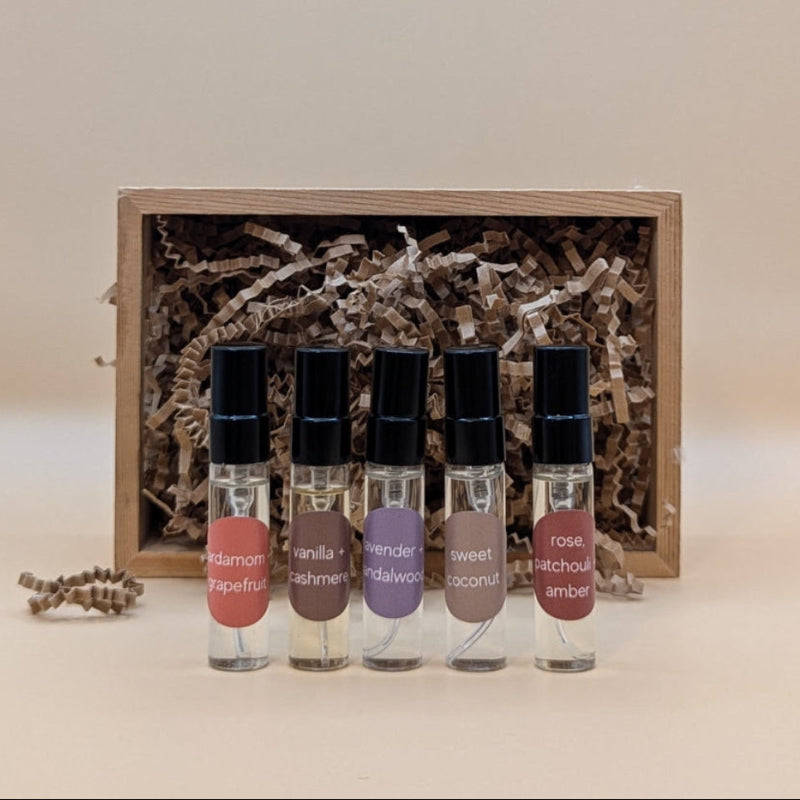 A discovery set featuring five samples of refillable plant based perfumes. The small glass vials have a black lids and each are labeled with a sticker. The gift box is brown paper and filled with craft paper. 