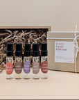 A discovery set featuring five samples of refillable plant based perfumes. The small glass vials have a black lids and each are labeled with a sticker. The gift box is brown paper and filled with craft paper. 