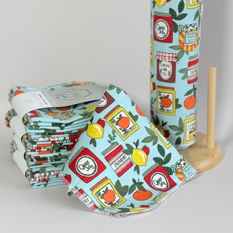 A stack of the Planet B Paperless Towels in the Jams & Jars pattern next to a roll of the same pattern on a towel roll holder. 