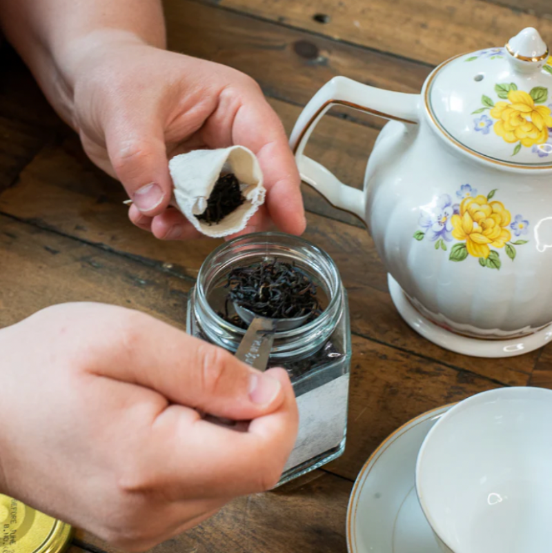 Hands holding a Planet B reusable tea bag folded open and scooping loose leaf tea in. 
