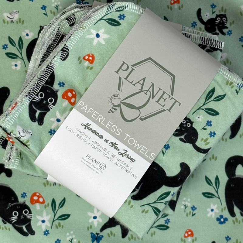 A stack of the Black Cat Patterned Paperless towels with the same patterned paperless towel in the background. 