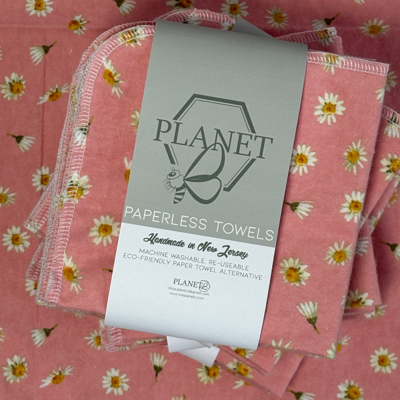A stack of the Pink Daisy patterned paperless towels with the same patterned paperless towel in the background. 