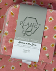 A stack of the Pink Daisy patterned paperless towels with the same patterned paperless towel in the background. 