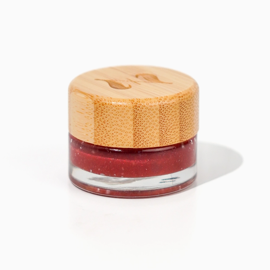 A small glass jar of Zerra &amp; Co. Cherry Flavored Plant Based Jelly with a light wooden lid rests on a white surface. The jelly is red with a shimmer. 